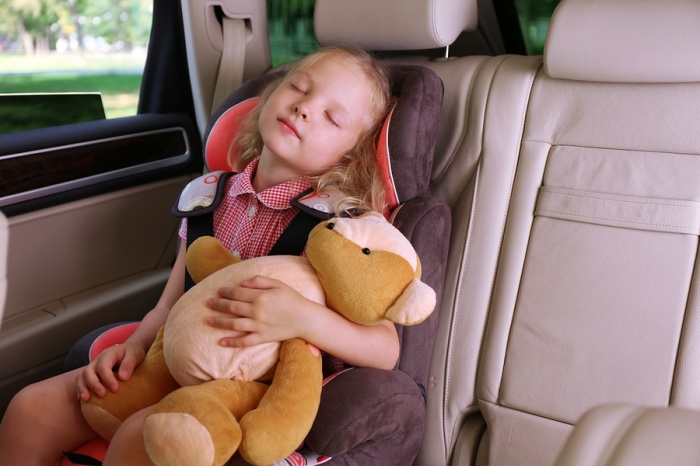 Beautiful happy girl with teddy bear sleeping in the car